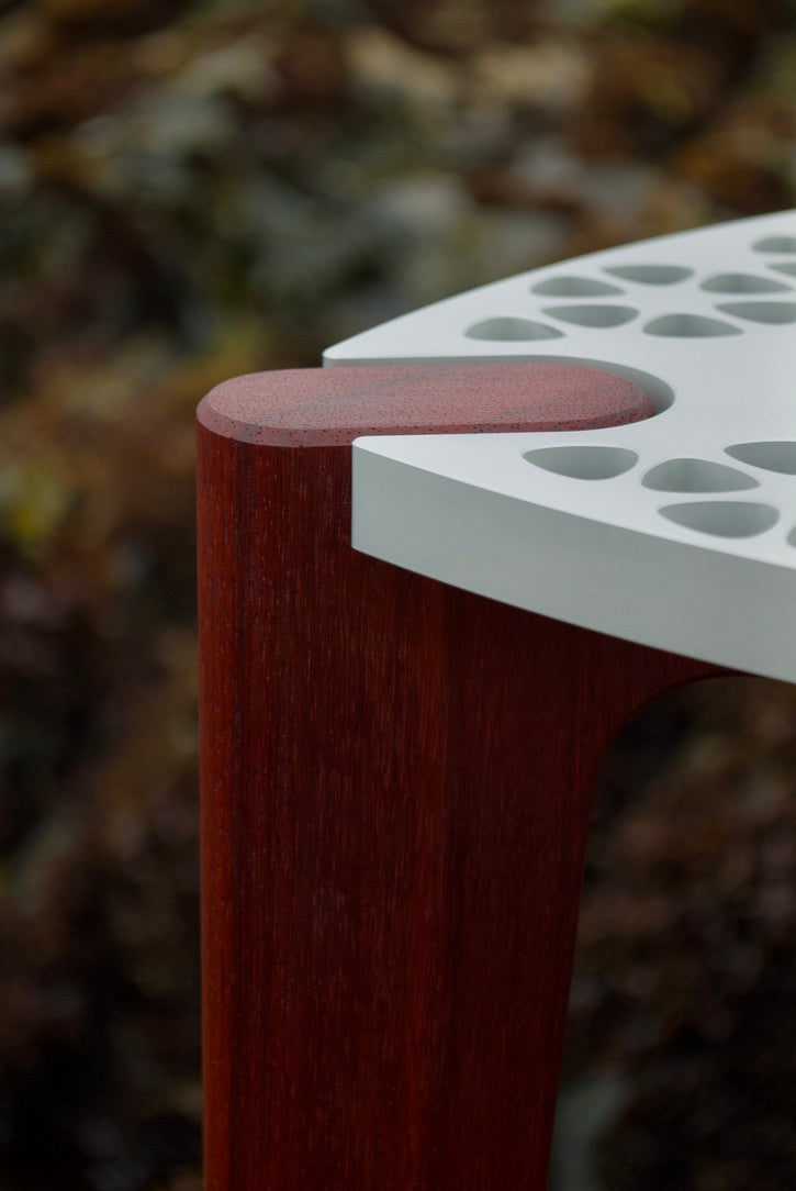 Modern minimalist designer stool/table with an aluminum top and red hardwood legs. Close up view of the top of one leg.