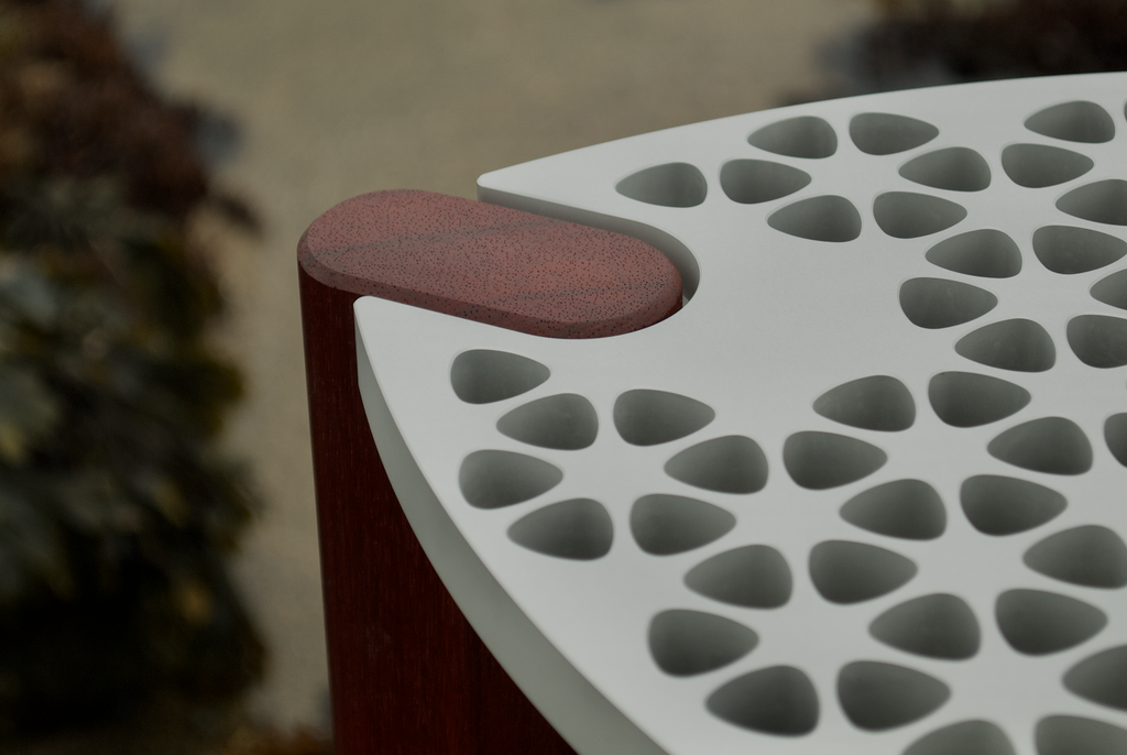 Modern minimalist designer stool/table with an aluminum top and red hardwood legs. Close op top-view of one corner of the seat.